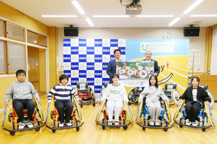 松本市長と日本財団の代表者と、車いすに乗った杭瀬小学校の児童たちが記念撮影をする様子
