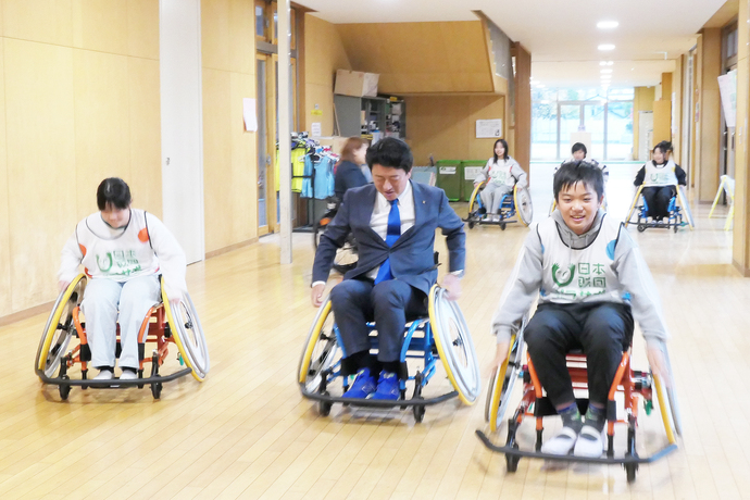 松本市長と児童たちが廊下で車いすに乗ってスピード競争をする様子